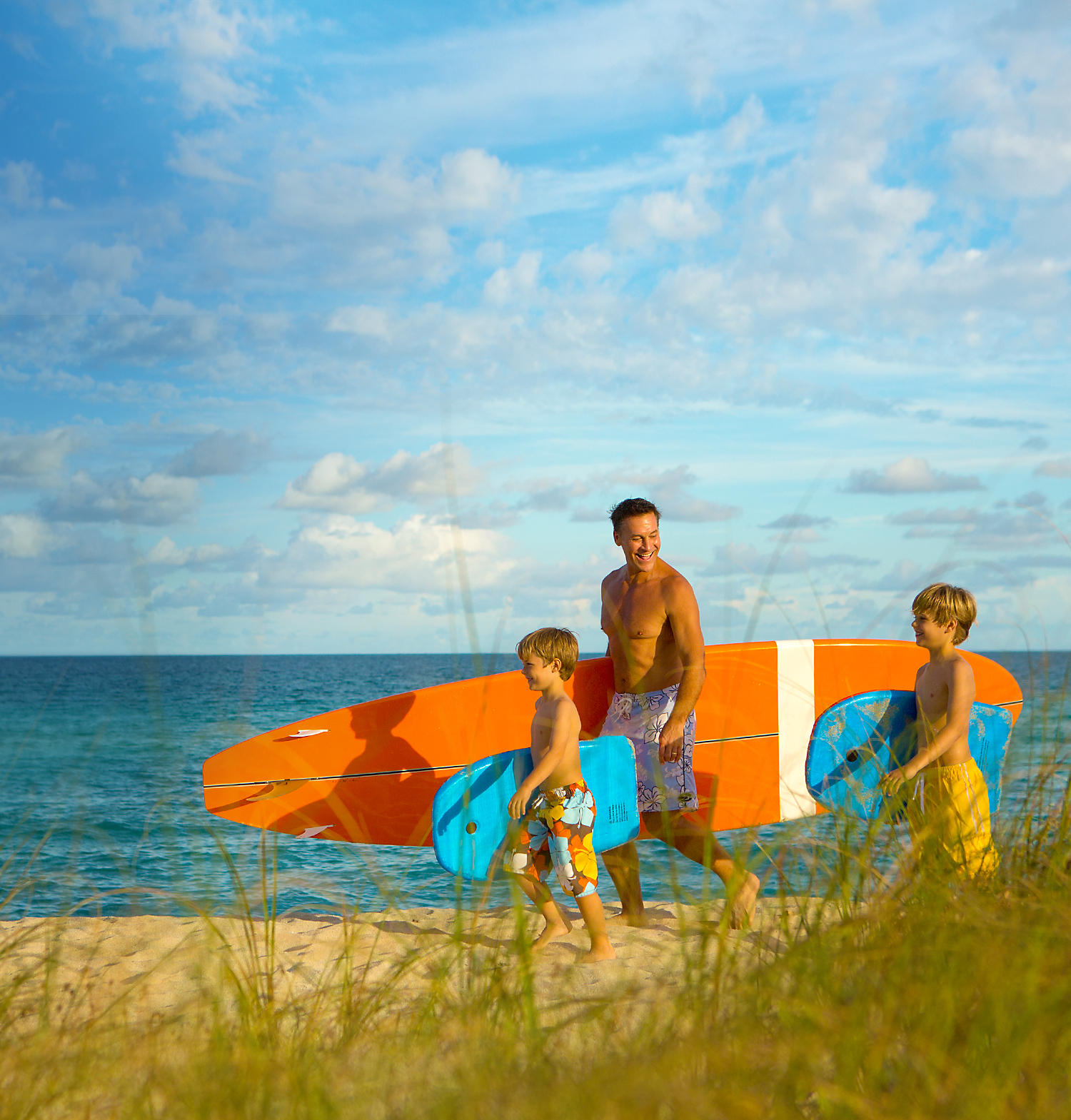 Father and his children holding surf boards heading towards the ocean.