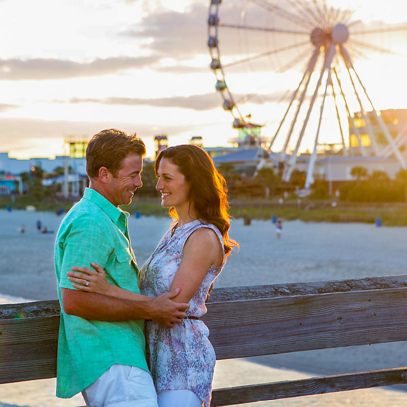 Couple of pier with Myrtle Beach SkyWheel in background at sunset