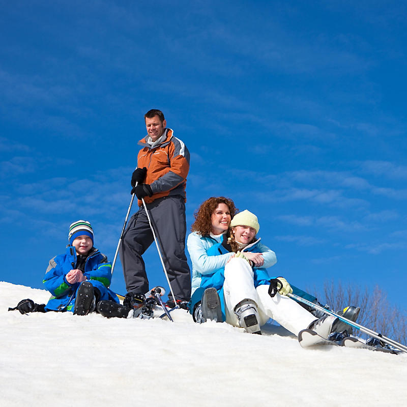 Man standing and lady and kids sitting on snow with skis
