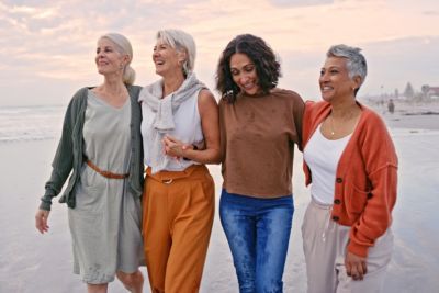 group of women walking on sand by ocean sunset