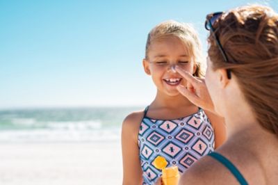 Mother applying sunscreen to daughter at beach
