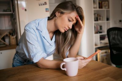 woman looking at mobile phone while coffee cup close by