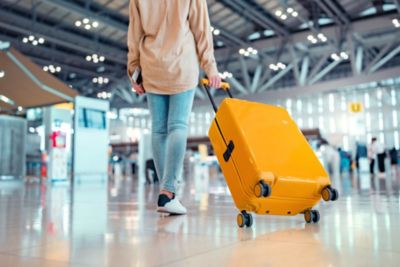 woman traveler passenger walking in airport with yellow suitcase